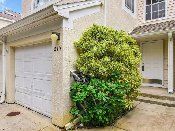 Front view of a house with a garage and entrance partially obscured by bushes.
