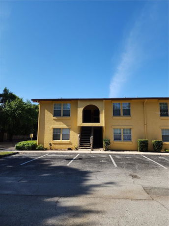 Front view of a two-story yellow apartment building with parking spaces in front.