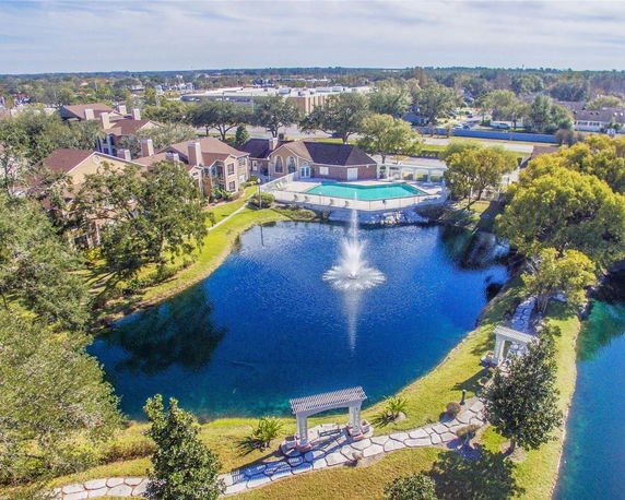 Panoramic view of a residential area with buildings, pool, and a pond with a fountain.