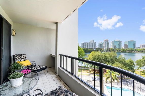 Balcony with chairs and a table overlooking a lake and city skyline.
