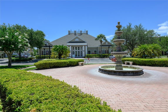 Front view of a building with large windows and a central entrance, surrounded by greenery and a fountain in the foreground.