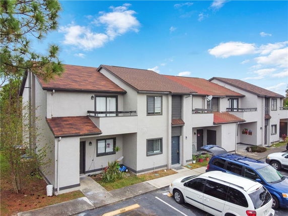 Front view of a multi-story townhouse with a brown roof and parking area in front.