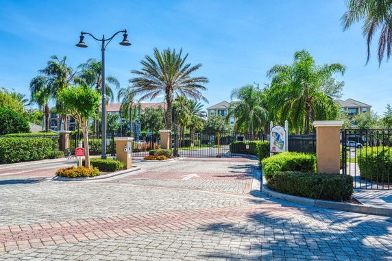 Front view of a gated residential complex with palm trees and multi-story buildings in the background.