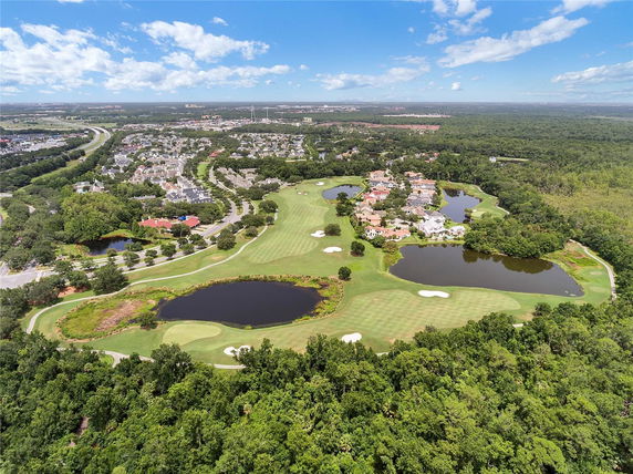 Panoramic view of a residential area with a golf course and several ponds, surrounded by trees and greenery.