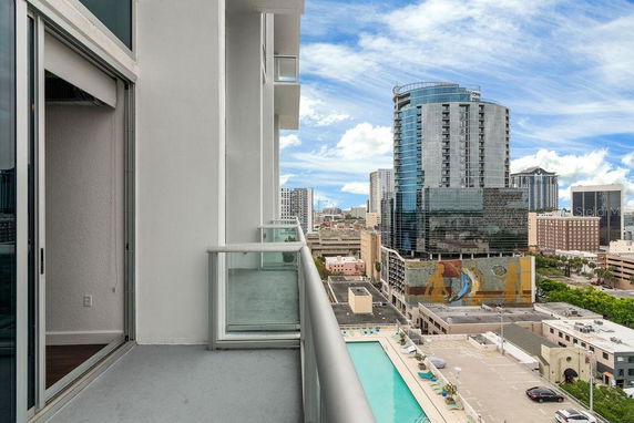 Panoramic view from a high-rise balcony overlooking an urban landscape with tall buildings and a swimming pool below.
