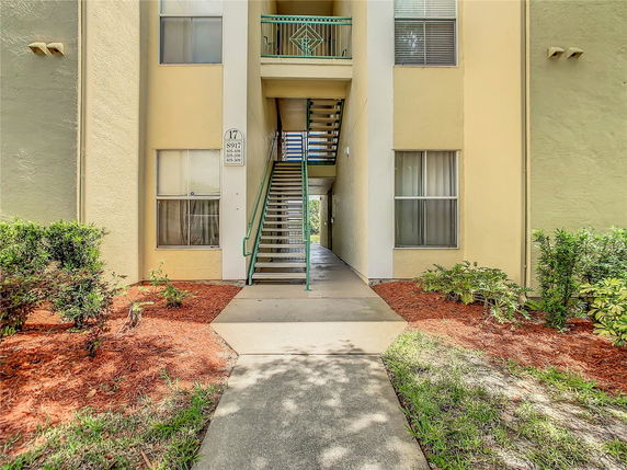 Front view of a multi-story building entrance with stairs and garden.
