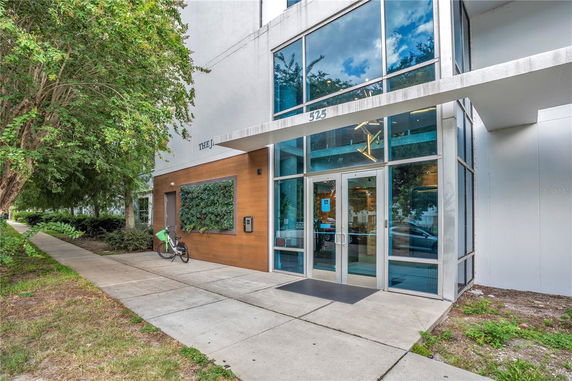 Front view of a modern building entrance with glass doors and greenery.