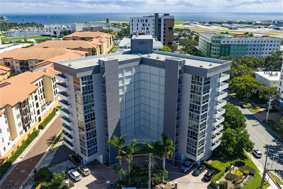 Front view of a multi-story building with a modern facade and surrounding cityscape including the ocean in the distance.