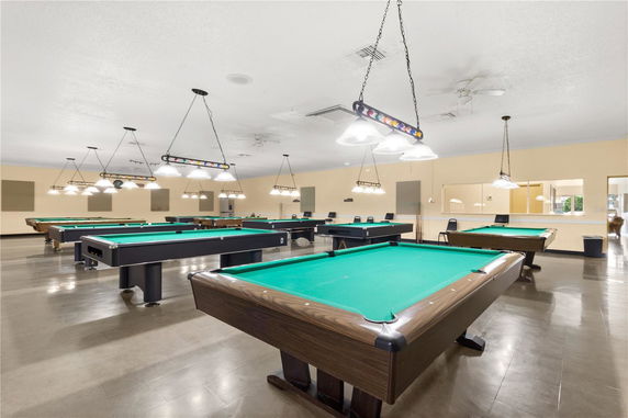 Indoor room with multiple billiard tables and hanging lights.