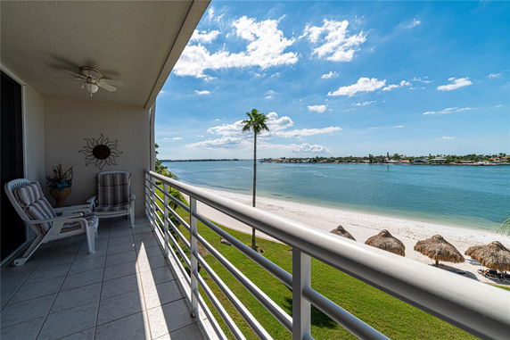 Balcony view overlooking a beach with thatched umbrellas and a body of water under a clear blue sky.
