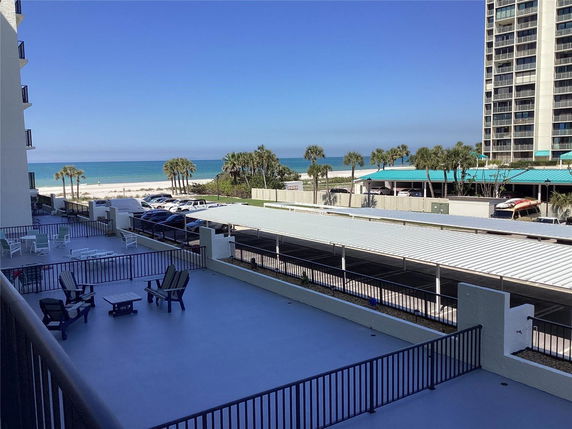 View of the ocean and beach from a building with a foreground of outdoor seating area and parking.
