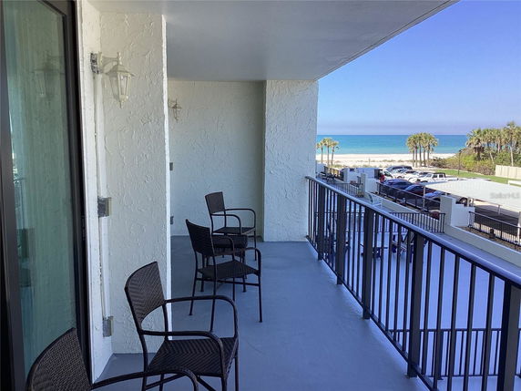 Balcony view overlooking a beach and ocean with chairs arranged.