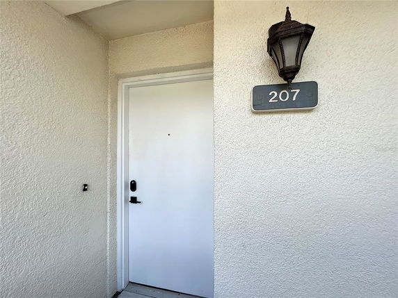 Front view of a door with a number 207 plaque and a wall-mounted light fixture.