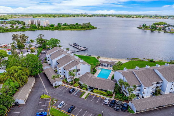 Aerial view of a lakeside residential complex with a swimming pool and parking, surrounded by greenery and overlooking a large body of water.