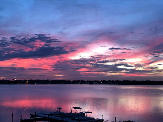 Panoramic view of a sunset over a lake with boats and a colorful sky.