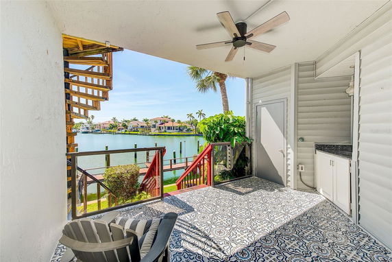 Covered outdoor patio with a ceiling fan overlooking a waterfront area with views of houses and palm trees.