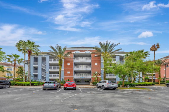 Front view of a multi-story building with balconies and a parking area in front.