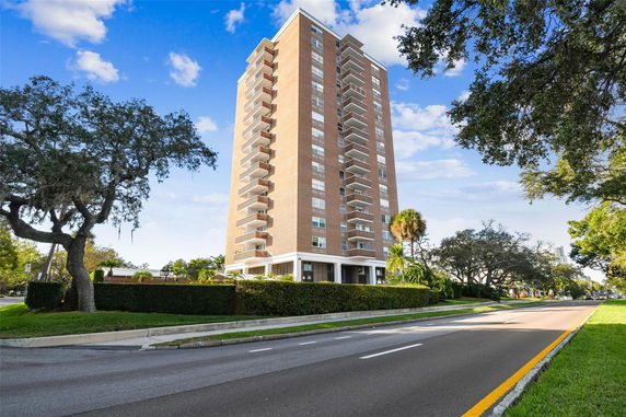 Front view of a tall, multi-story building with balconies and surrounding greenery.