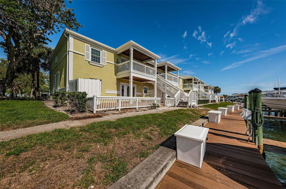 Front view of a two-story yellow building with a balcony and stairs, located next to a wooden dock.