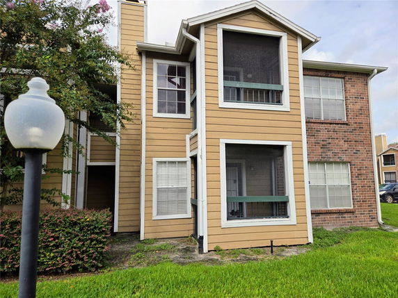 Front view of a two-story apartment building with screened balconies and a combination of wooden and brick exterior.