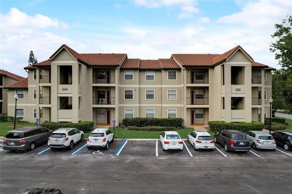 Front view of a three-story apartment building with a tiled roof and multiple parked cars in front.