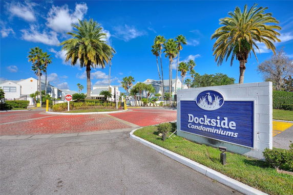 Front view of a condominium complex entrance with a sign and palm trees.