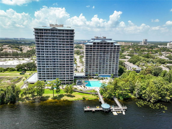 Front view of two high-rise buildings with a pool area in front, situated by a body of water.