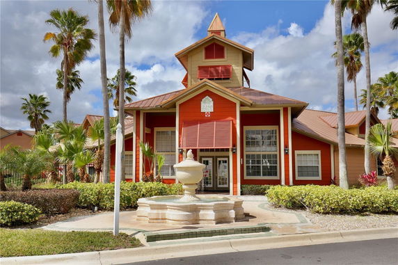 Front view of a brightly colored house with a fountain and palm trees.