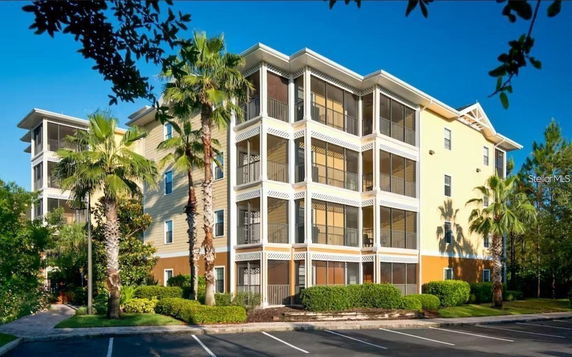 Front view of a multi-story residential building with screened balconies and surrounding palm trees.