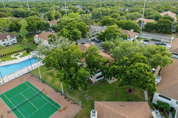 Aerial view of residential buildings with a swimming pool and tennis court, surrounded by lush green trees.