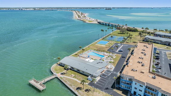 Panoramic view of a waterfront area with buildings, a pier, tennis courts, and swimming pools.