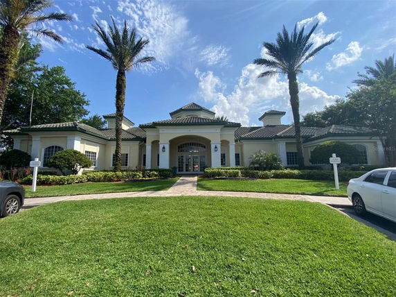 Front view of a large house with a tiled roof, palm trees, and a well-maintained green lawn.
