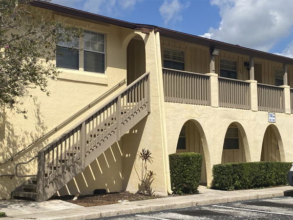 Front view of a two-story building with outdoor stairs and arched columns.