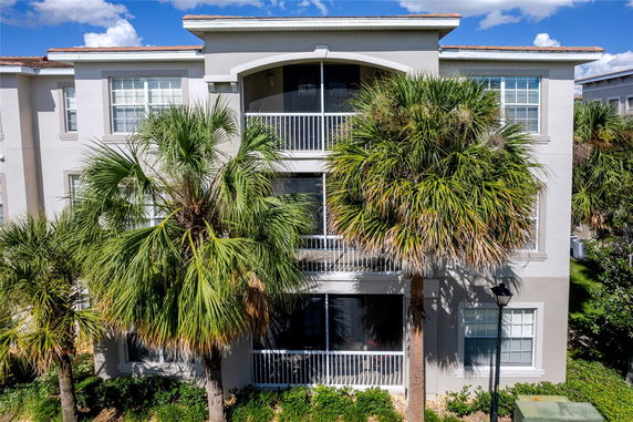 Front view of a three-story residential building with balconies and palm trees.