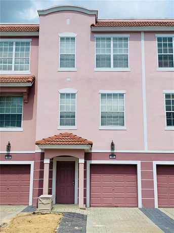 Front view of a three-story building with a pink exterior and two garages.