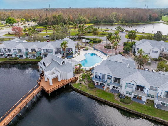 Aerial view of a residential area with white buildings surrounding a central swimming pool, located by a lake.