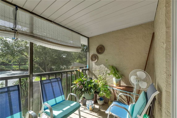 View from a balcony with chairs, plants, and a fan, overlooking trees and a pathway.