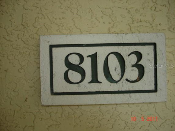Close-up of a number plate displaying the number 8103 on a textured wall.