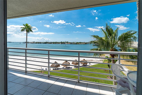 Balcony view overlooking a beach with palm trees and a distant shoreline.