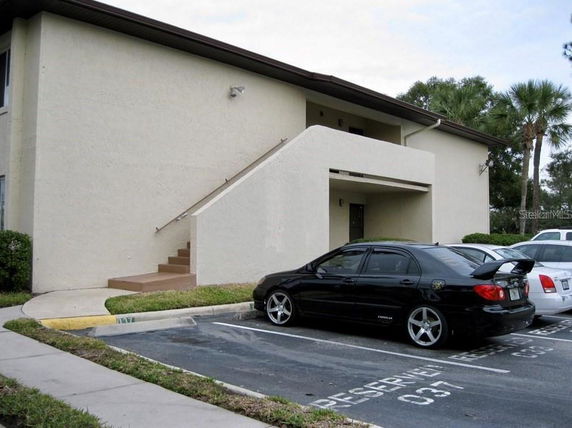 Front view of a two-story building with an external staircase and parking area.