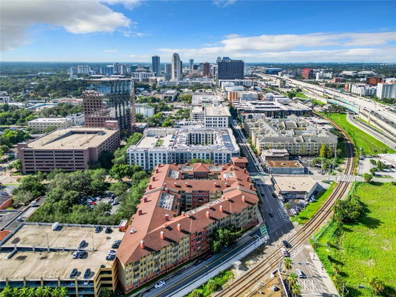 Aerial panoramic view of a cityscape featuring multiple buildings, roads, and green areas under a blue sky.