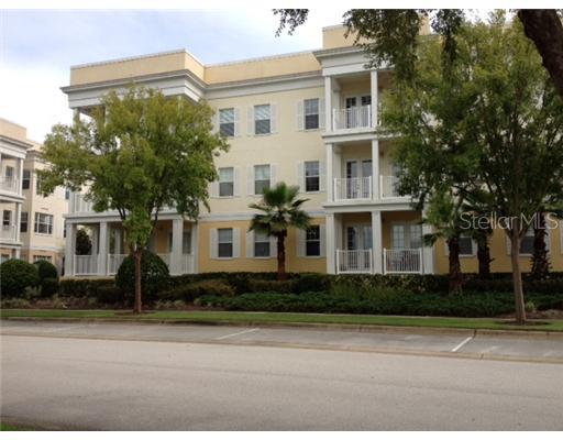 Front view of a three-story apartment building with balconies and trees in front.