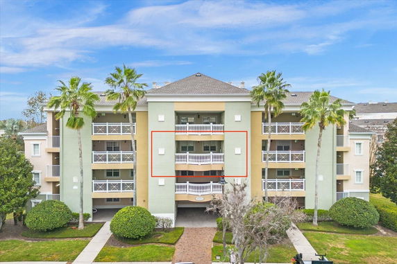 Front view of a multi-story apartment building with balconies and palm trees.