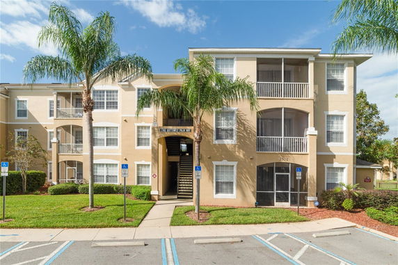 Front view of a multi-story residential building with balconies and palm trees.