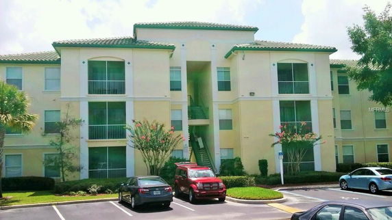 Front view of a three-story apartment building with balconies and a tiled roof.