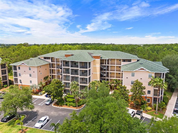 Front view of a multi-story apartment building with a green roof and balconies, surrounded by trees.