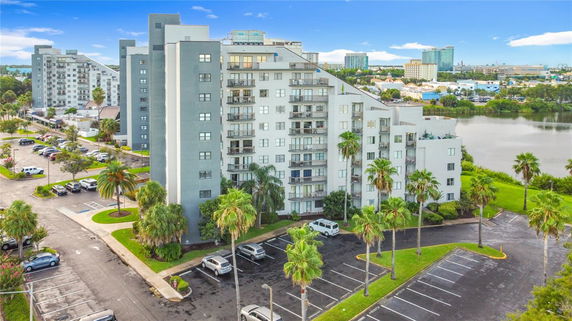 Front view of a multi-story apartment building with balconies and surrounding parking area.