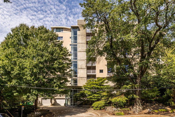 Front view of a multi-story building with a glass elevator shaft and surrounded by trees.
