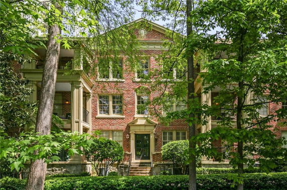 Front view of a multi-story red brick building with columns and greenery.