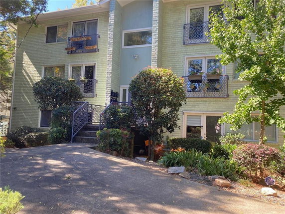 Front view of a multi-story residential building with balconies and stairs, surrounded by greenery.